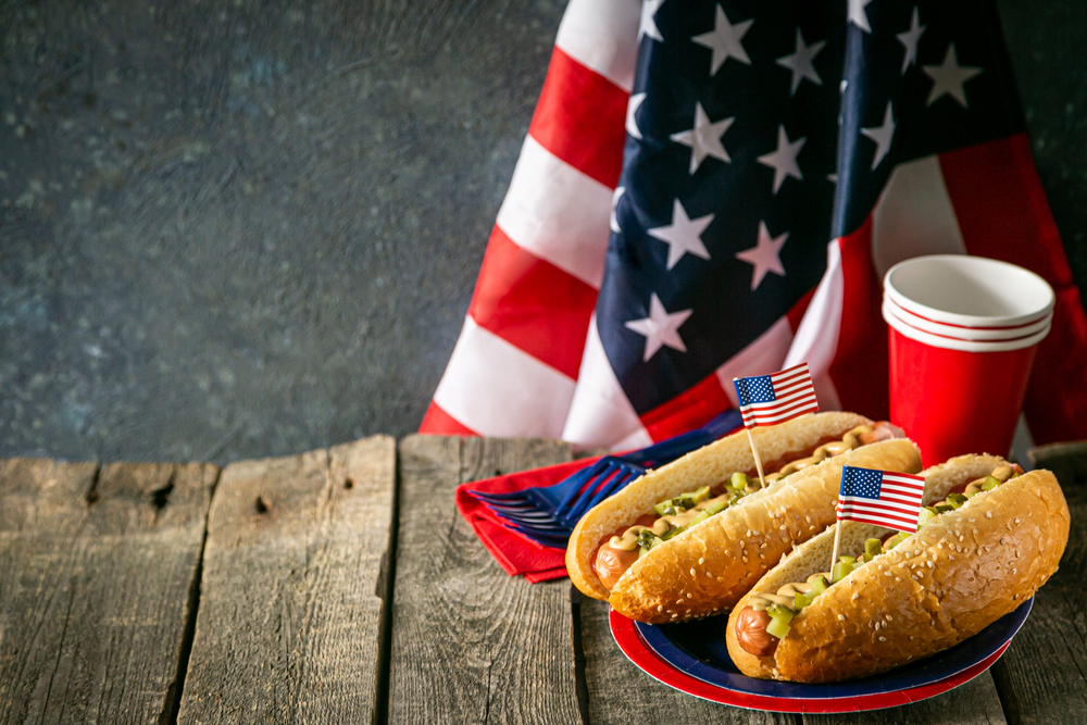 Memorial Day hotdogs on a red and blue plate look delicious in front of an American flag as a fun dog party idea for this celebrated American holiday.