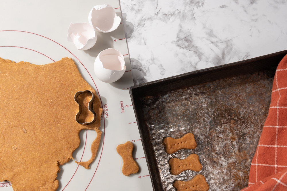 Making homemade dog treats is shown with a bone-shaped cookie cutter and baking sheet.